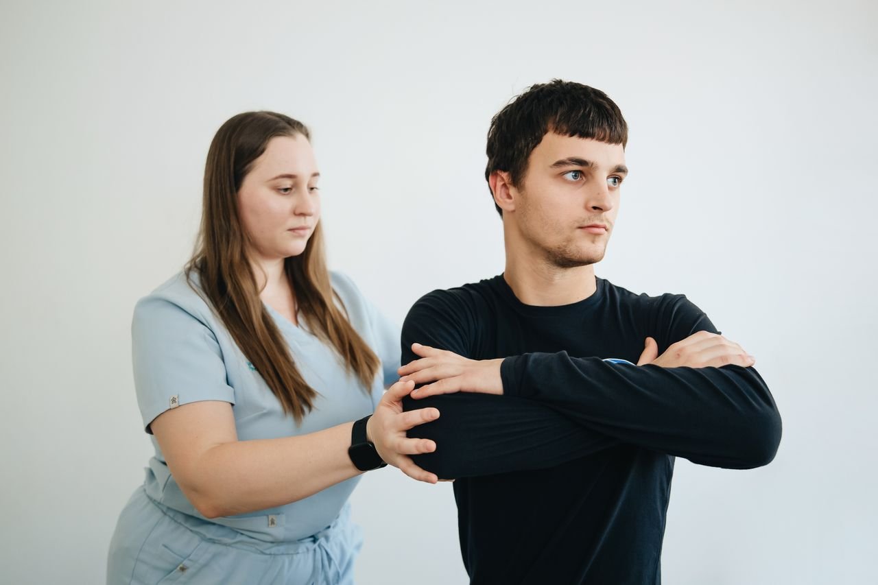 A physiotherapist assists a patient with arm exercises in a clinical setting.